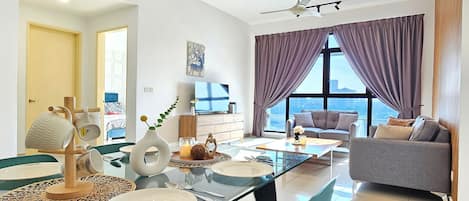 A modern living room with a glass dining table, a sofa, and a large window with purple curtains.
