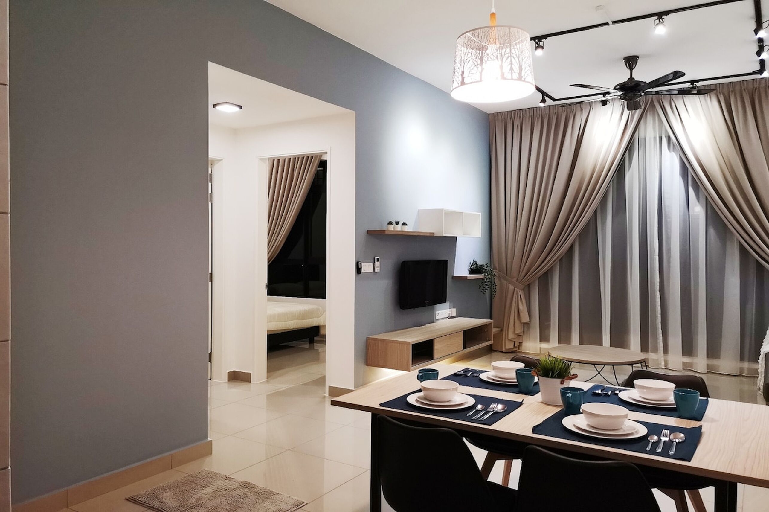 A modern dining area with a table set for four, a television on the wall, and a ceiling fan.