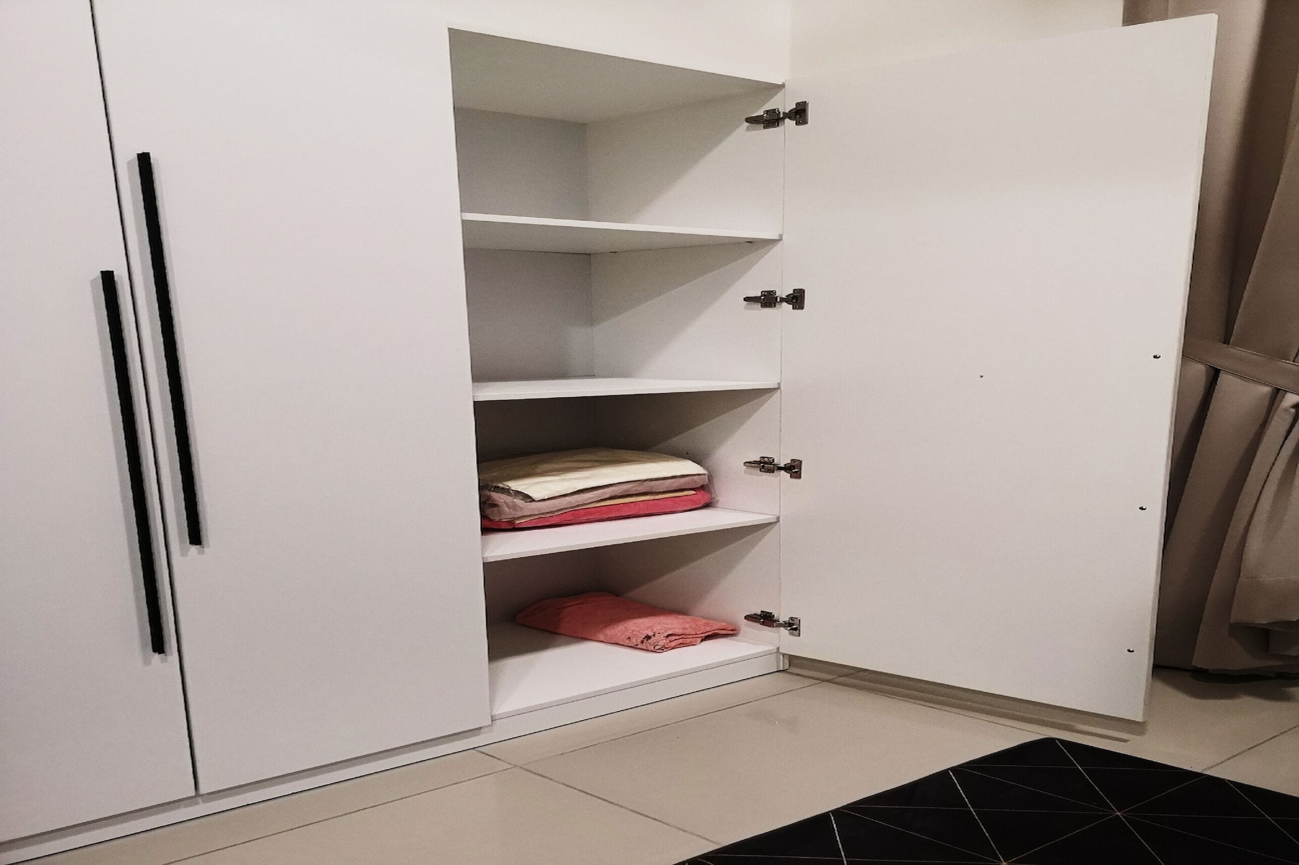Un armario blanco con varios estantes y una barra para colgar, con una alfombra estampada en blanco y negro en el suelo.
