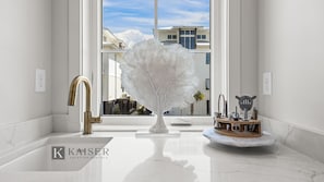 Ein modernes Badezimmer mit einem weißen Marmorbecken, einem goldenen Wasserhahn und einer einzigartigen weißen Skulptur in Form eines Baumes.