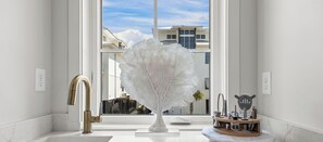 Une salle de bain moderne avec un lavabo en marbre blanc, un robinet doré et une sculpture d’arbre blanche originale qui sert de pièce maîtresse.