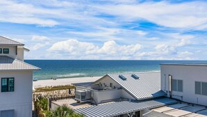 Une propriété située en bord de mer, avec vue sur la plage, un toit équipé de panneaux solaires et un ciel dégagé.