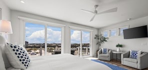 A spacious bedroom with a large bed, a ceiling fan, and a view of the city through large windows. - Pelican Bluff, a premier beachside home. Private pool and elevator by Kaiser Vacations (Orange Beach)