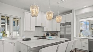 Une cuisine moderne avec des meubles blancs, un îlot central et un réfrigérateur en acier inoxydable.