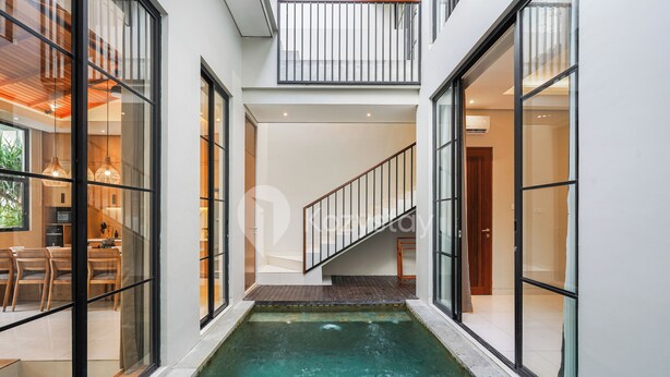 A modern interior with a central water feature, glass doors, and a staircase leading to an upper level. - Lucenta Villa by Kozystay - Canggu (Canggu)