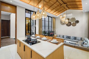 Una cucina moderna con isola centrale, pensili in legno e piano cottura integrato. C'è un'area pranzo con un divano e una TV.