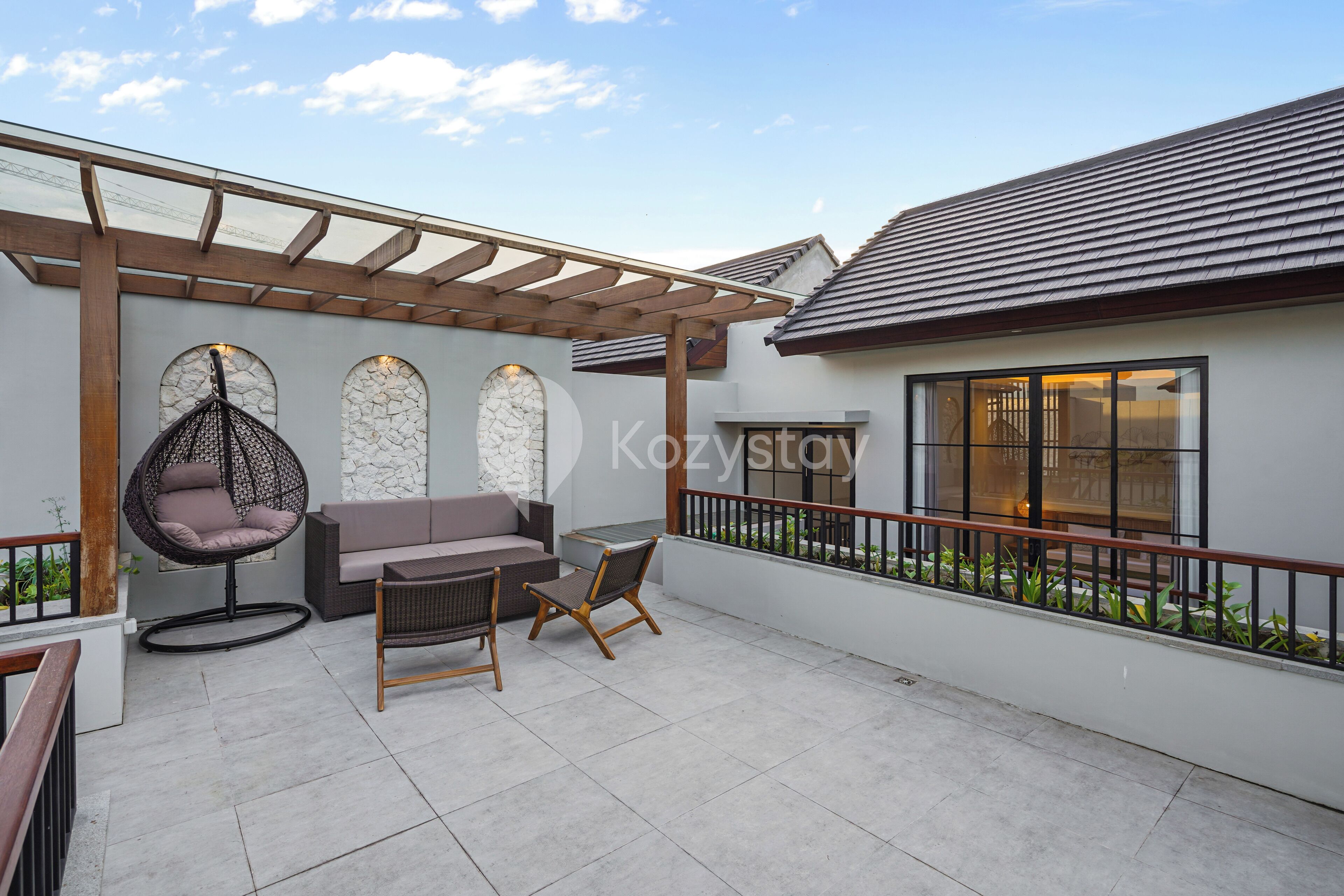 Ein überdachter Patio-Bereich mit gepolstertem Sessel, einer Couch und zwei Holzstühlen.