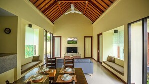 A spacious living area with a high ceiling, a dining table set for four, a sofa, and a television.