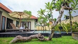 A poolside area with lounge chairs, a large umbrella, and a tree.