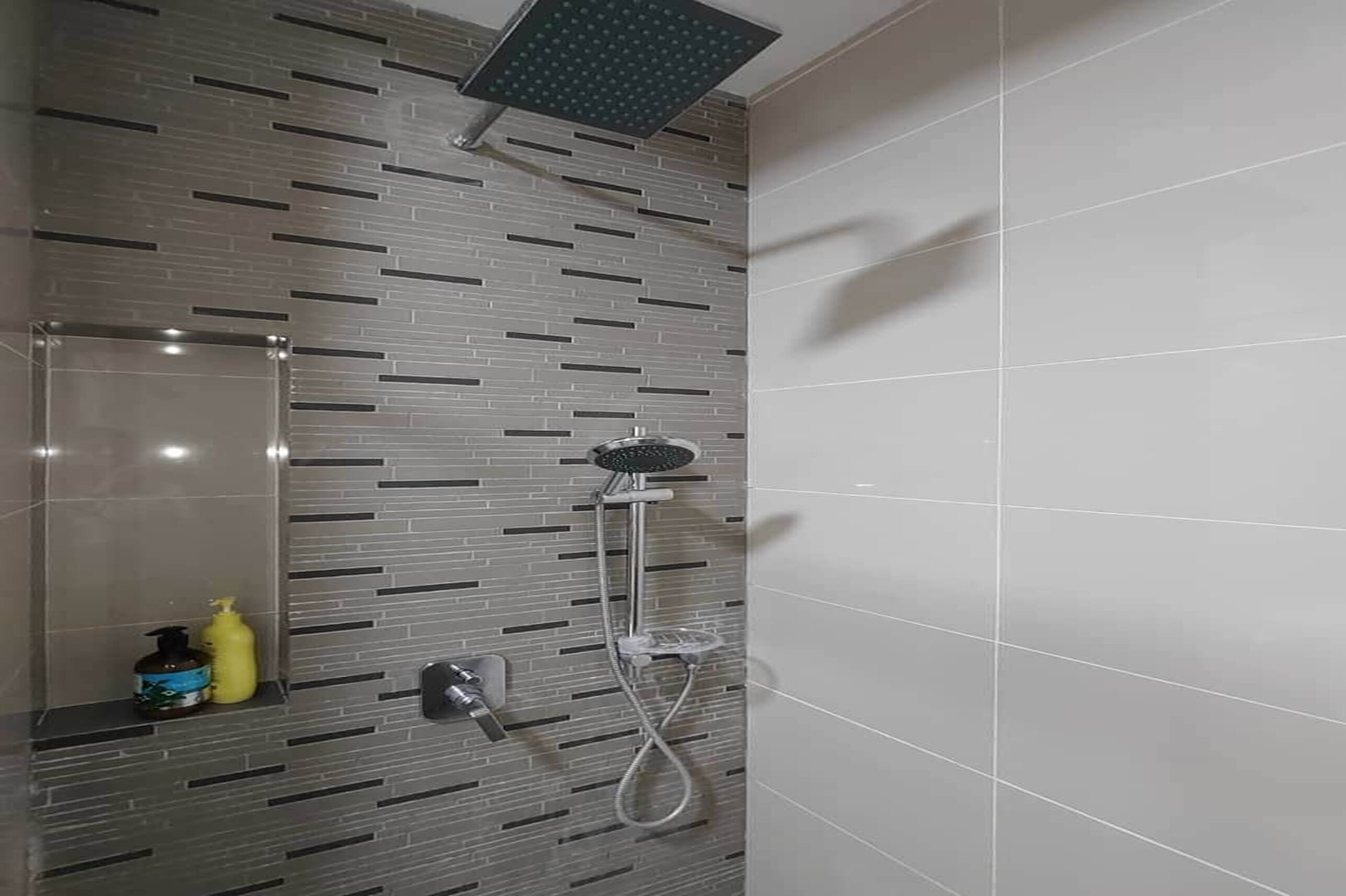 A modern bathroom with a shower, a mirror, and a shelf with toiletries.