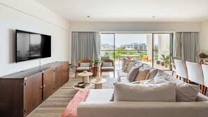 Una sala de estar moderna con televisor de pantalla plana, sofá, sillas, comedor y balcón con vista a la ciudad.