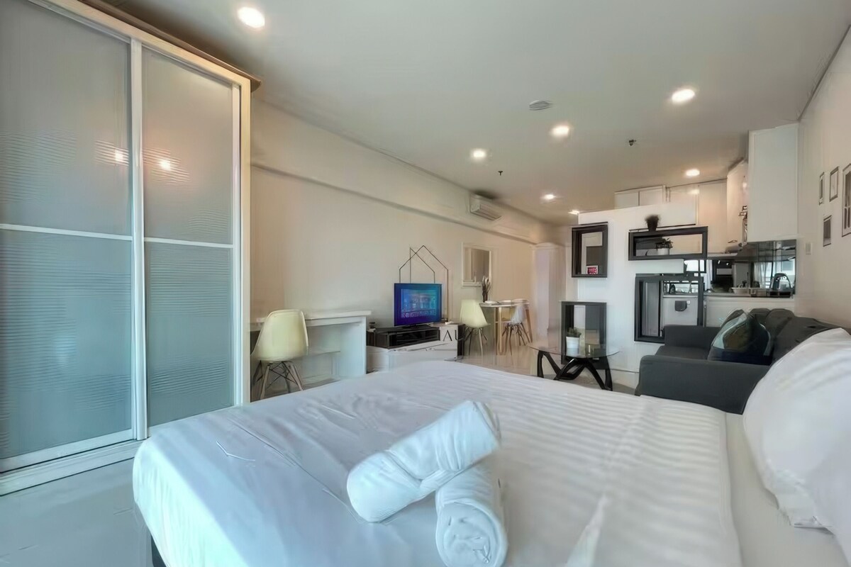 A hotel room with a bed, a desk, a chair, a TV, and a kitchenette.