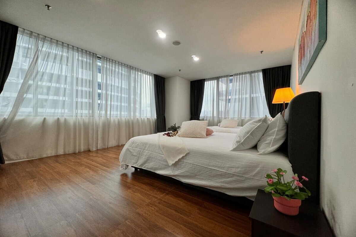 A bedroom with a large bed, a bedside table with a lamp, and a potted plant.