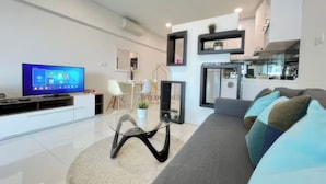 A modern living room with a flat-screen TV, a sofa with cushions, a coffee table, and a dining area with chairs. - Mercu Summer Suites KL Lifestyle (Kuala Lumpur)