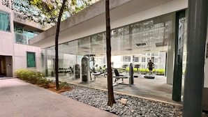 An outdoor gym area with exercise equipment, a stone pathway, and a glass wall reflecting the gym. - Mercu Summer Suites KL Lifestyle (Kuala Lumpur)