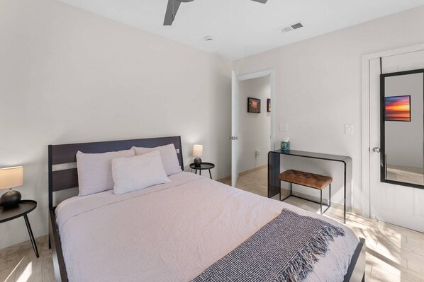 A modern hotel room with a large bed, bedside tables, a bench, and a door with a view.