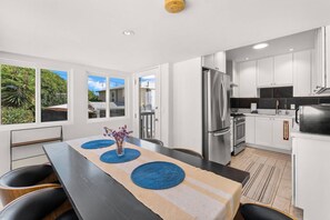 A modern kitchen with stainless steel appliances, a dining area with a table set for four, and large windows offering a view of the outdoors.