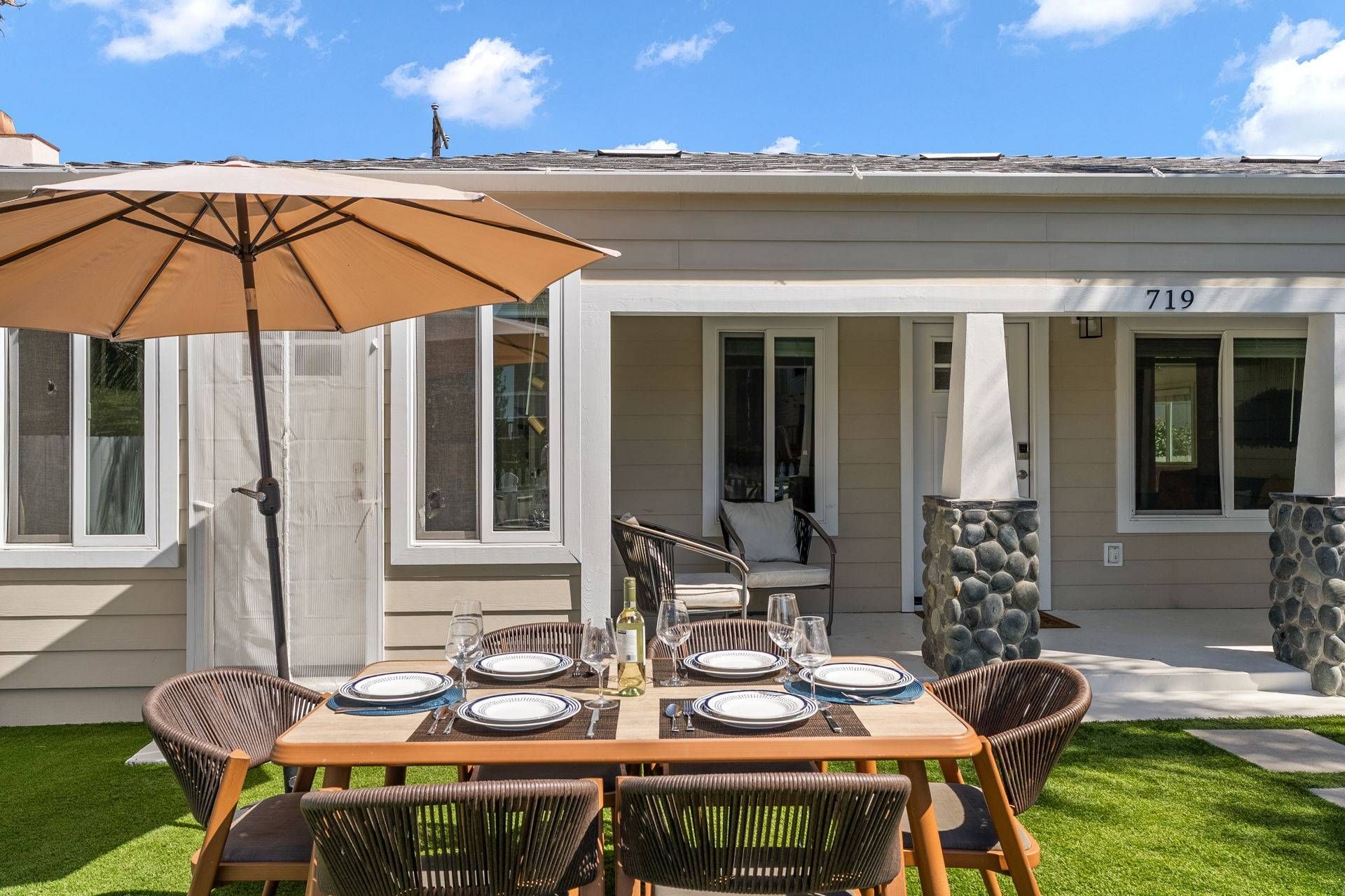 Een terras met een eettafel, buitenzitplaatsen en een grote parasol.