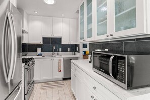A modern kitchen with white cabinetry, a stainless steel refrigerator, a microwave, and a gas stove. - Walk to Moonlight Beach, Updated and Remodeled, Dream Getaway (Encinitas)
