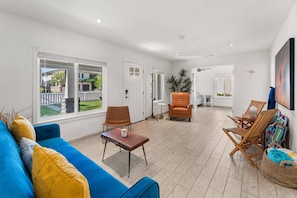 A spacious living area with a blue sofa, a wooden coffee table, and a large window offering a view of a fenced garden. - Walk to Moonlight Beach, Updated and Remodeled, Dream Getaway (Encinitas)