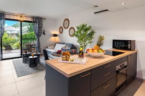 Une cuisine moderne avec un plan de travail en bois, un four à micro-ondes et un évier. On y trouve un coin repas avec une table et des chaises, ainsi qu’une grande fenêtre agrémentée de rideaux.