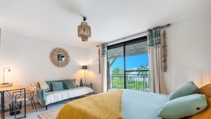 Une chambre moderne avec un grand lit, un bureau et un canapé. Elle dispose d’un balcon avec vue sur la verdure.
