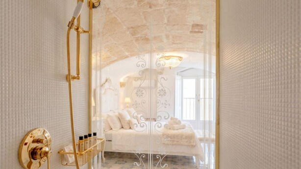 A room with a bed, a glass shower enclosure, a white wall with a textured pattern, and a patterned floor. - Ducale – Historic Charm and Comfort in the Heart of Monopoli (Monopoli)