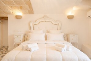 Una cama con dosel blanco, adornada con toallas enrolladas, dos mesitas de noche y apliques de pared.