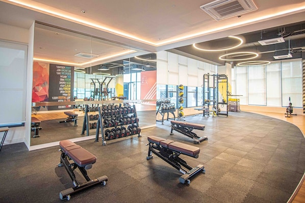 Un gimnasio moderno con cintas de correr, mancuernas, bancos y máquinas de pesas.
