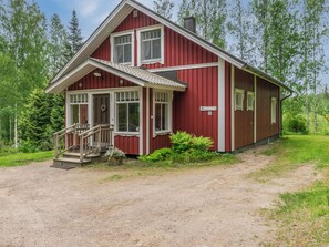 Ein rotes Holzhaus mit Veranda, Treppe und einer Auffahrt aus unbefestigtem Weg.