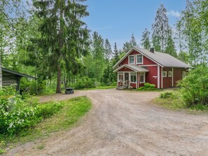 A red house with a gravel driveway, surrounded by greenery and trees.