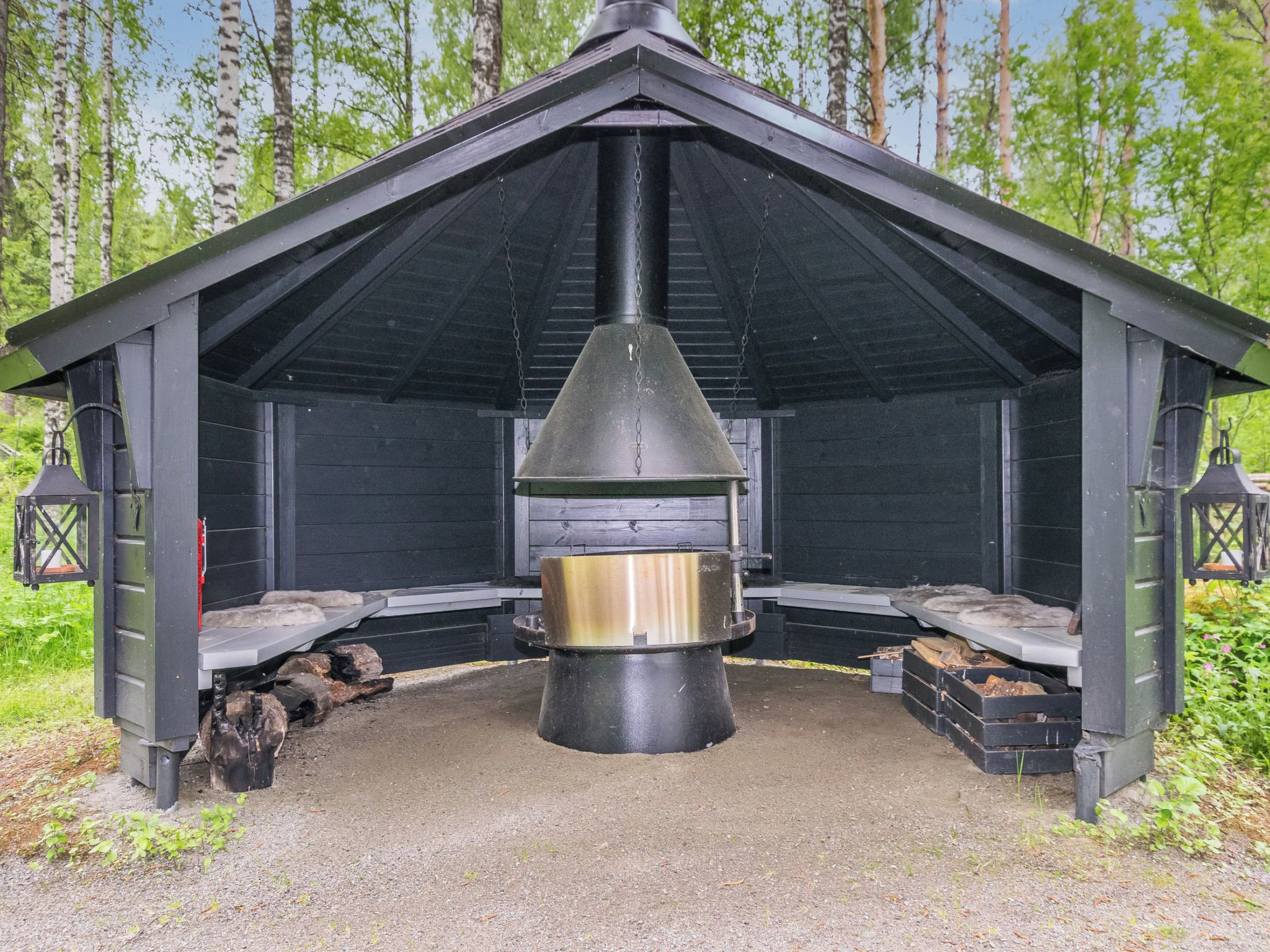 A black wooden structure with a conical chimney, benches, and lanterns.