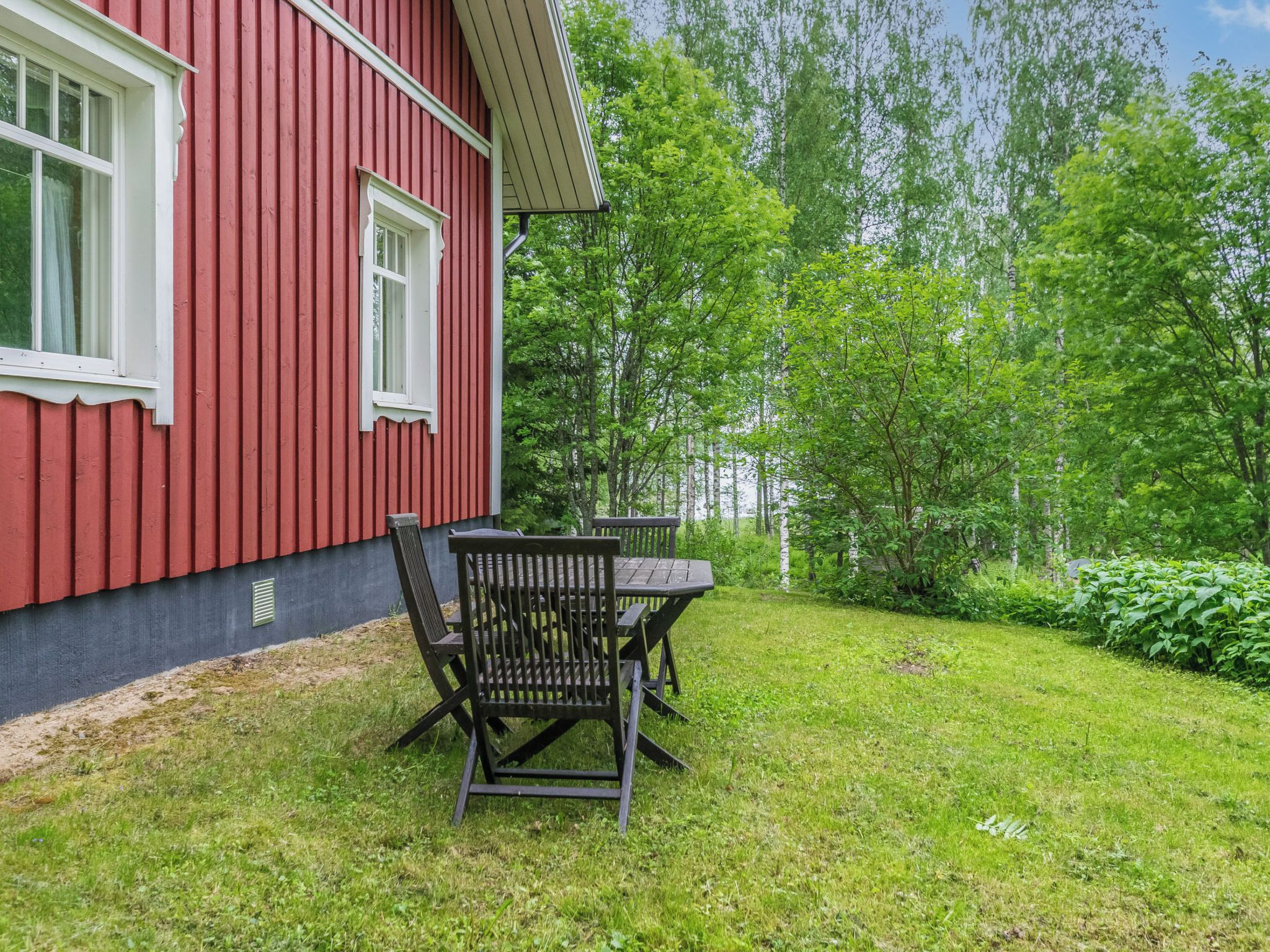 En rød bygning med et vindue og borde med stole i gården.