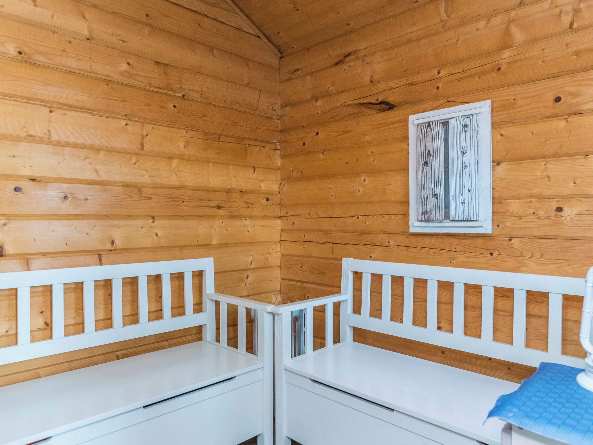 L’intérieur d’une cabane avec des murs en bois, deux bancs blancs et un tableau encadré accroché au mur.