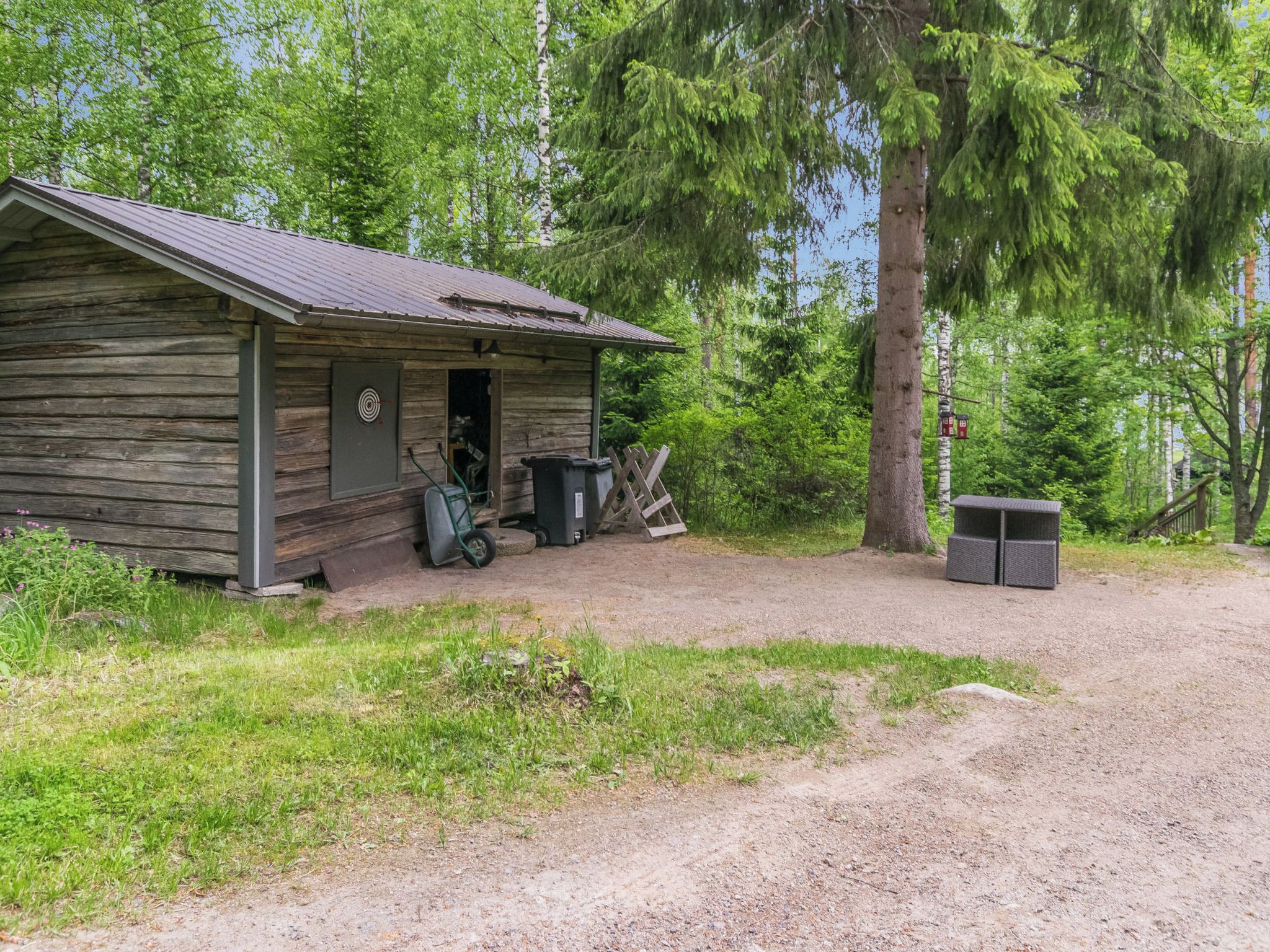 Una cabana rústica amb un camí de terra que hi mena, envoltada d'un bosc dens.