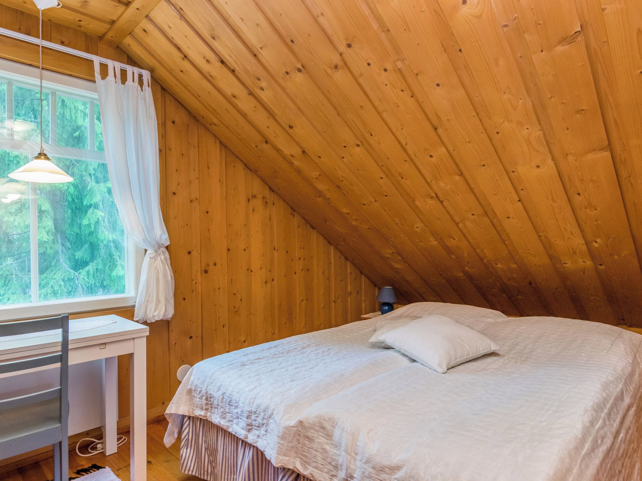 Un dormitorio con cama, escritorio y ventana con cortinas.