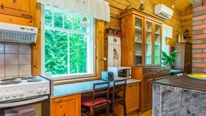 Cocina estilo cabaña acogedora, con armarios de madera, estufa, microondas y un amplio ventanal con vistas a la vegetación.
