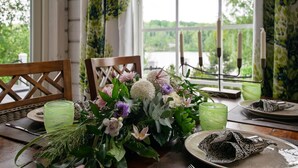 Une table dressée pour le dîner, avec vue sur un lac, un chandelier et un arrangement floral en guise de centre de table.