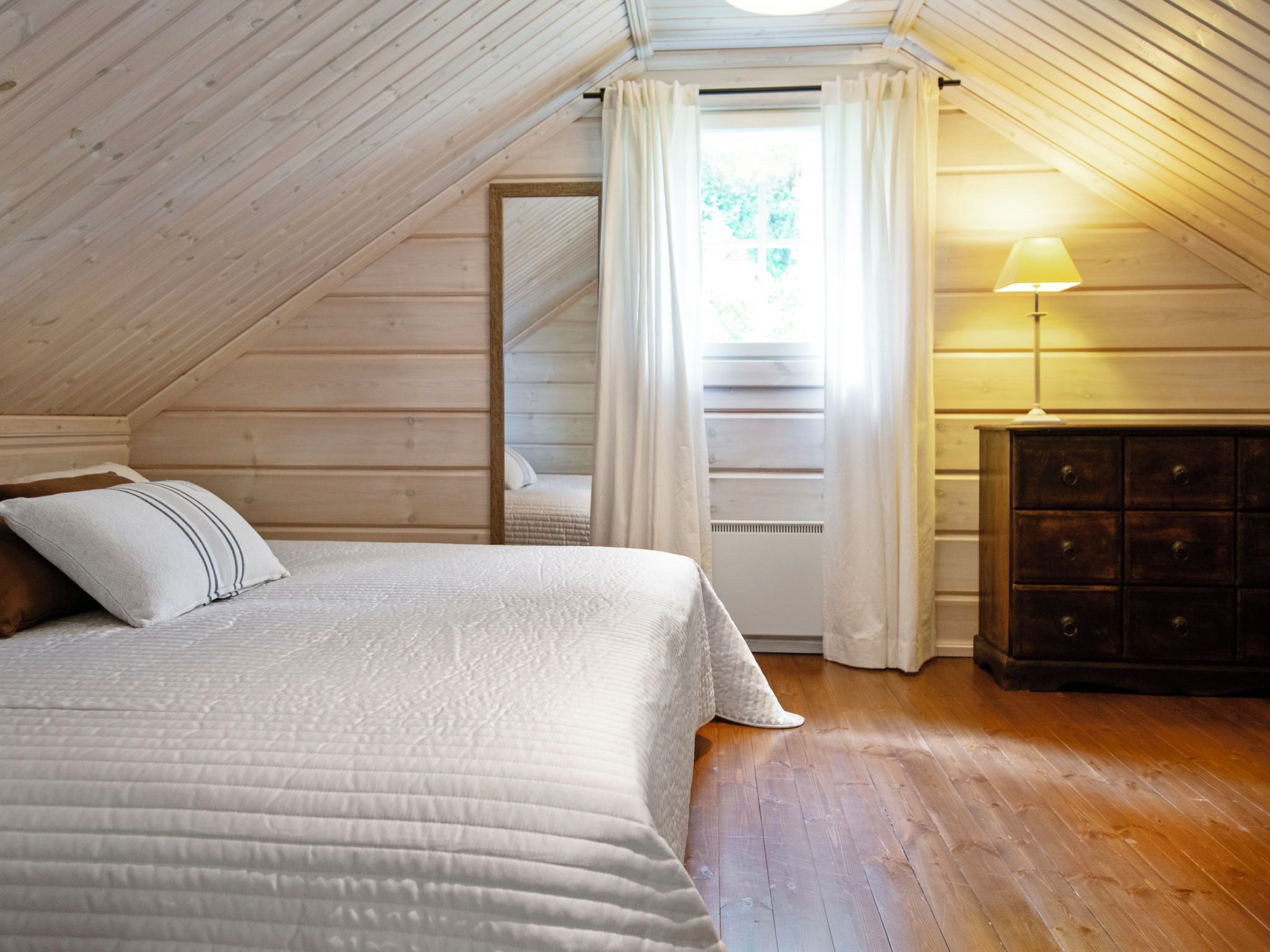 Une chambre à coucher avec un lit, une commode et une fenêtre avec des rideaux.