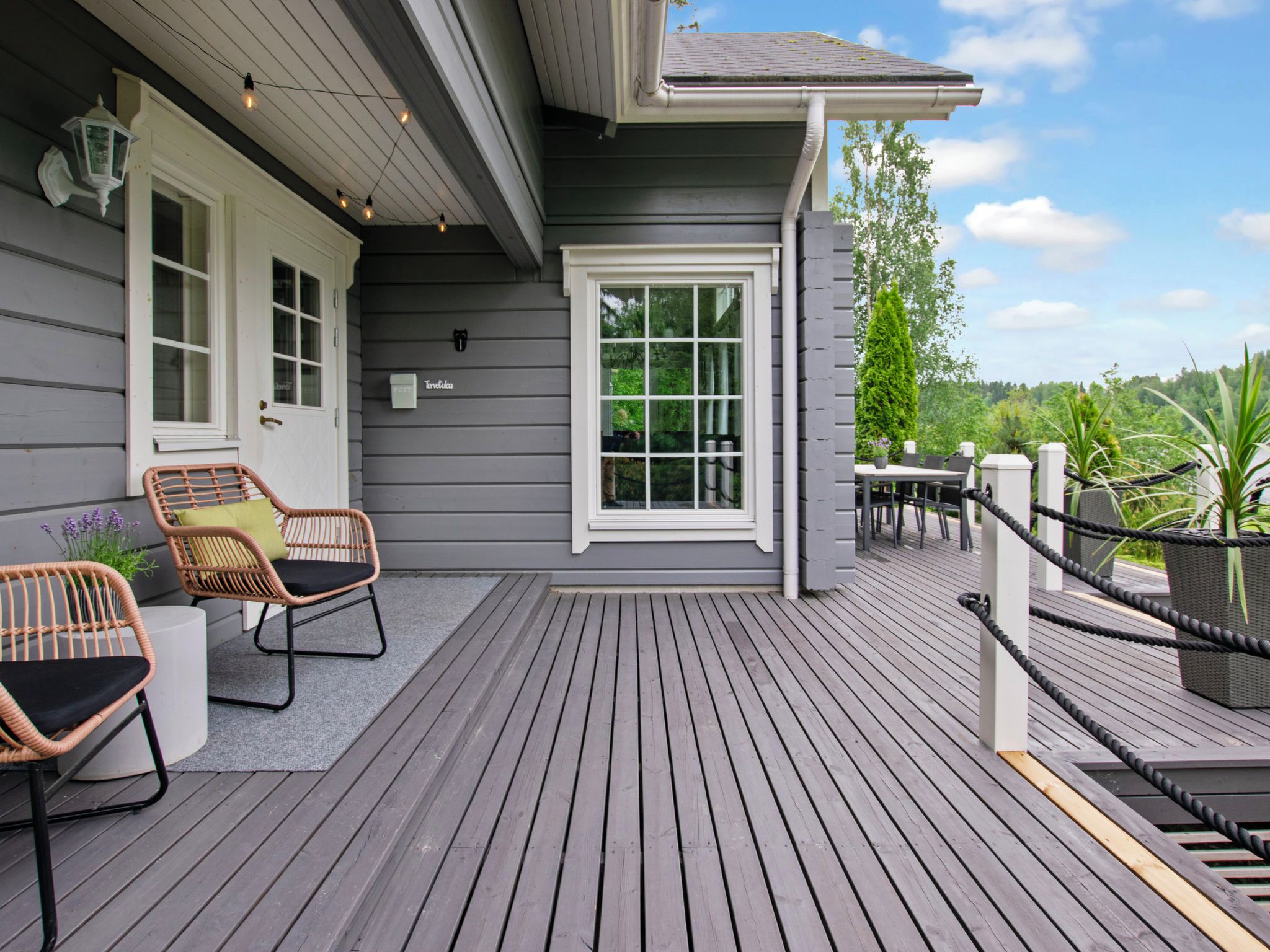 Une terrasse en bois avec des meubles d’extérieur, une boîte aux lettres et une vue sur la végétation environnante.