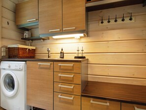 A kitchen with wooden cabinets, a washing machine, and a soap dispenser on the counter. - Aurinkoranta by Interhome (Ikaalinen)