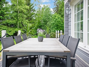 A rectangular wooden table with six chairs, surrounded by greenery and a white fence.