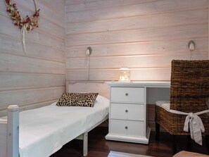 Une petite chambre avec un lit simple, un mur en bois, une table de chevet avec une lampe, une chaise et une décoration murale.