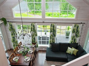 Un coin repas avec une table dressée pour quatre personnes, un canapé et une vue sur un jardin grâce à de grandes fenêtres.