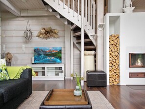 Una sala moderna con una escalera de madera, un televisor de pantalla plana, una chimenea y un rincón de descanso acogedor.