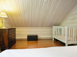 A room with a sloped ceiling, a wooden dresser, a small black box, a crib, and a bed with a white quilt. - Aurinkoranta by Interhome (Ikaalinen)