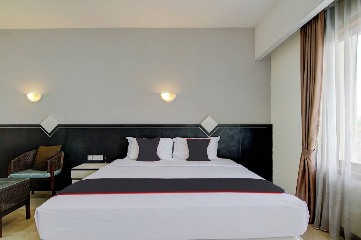 A hotel room with a large bed, two wall-mounted lights, a chair, and a window with curtains.
