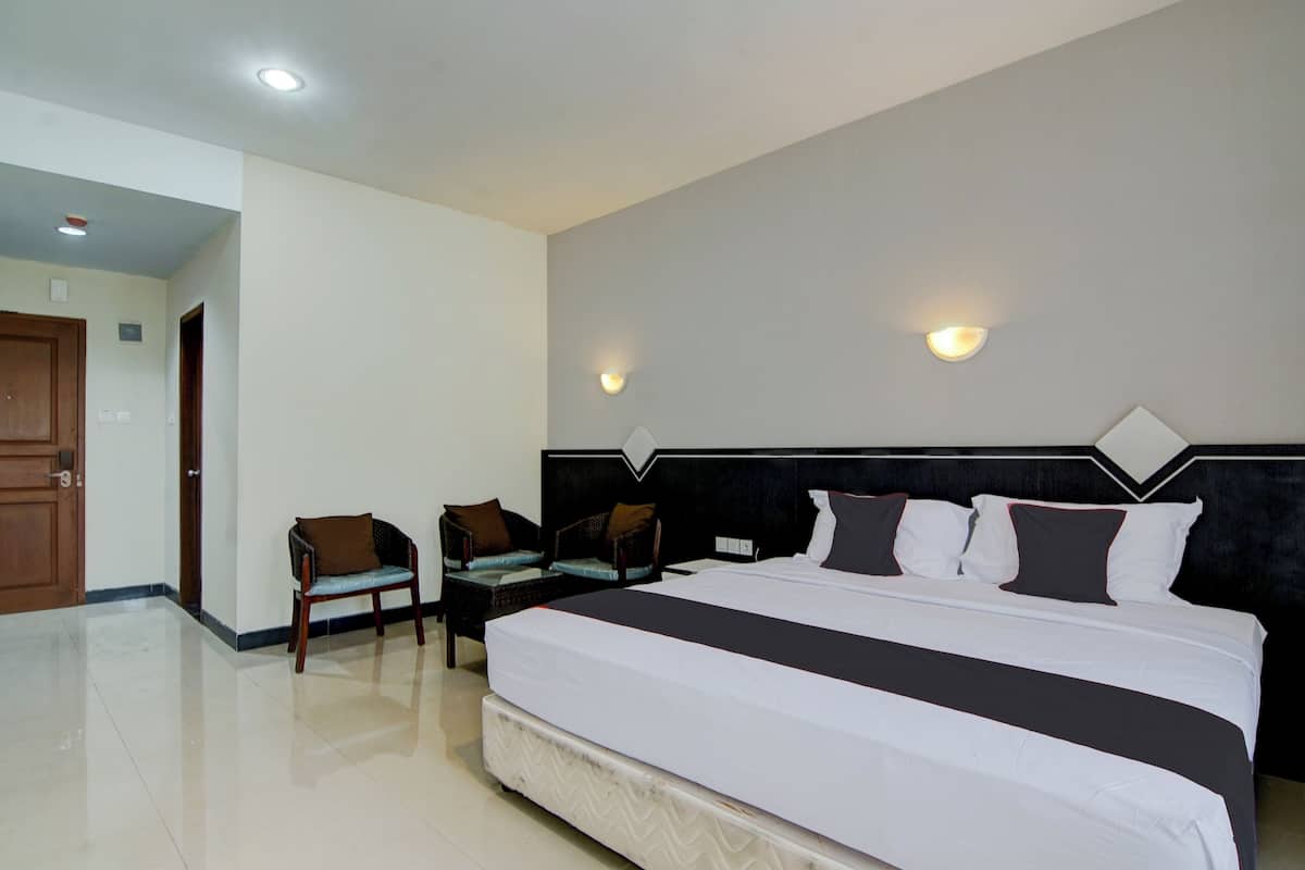 A hotel room with a large bed, two chairs, a nightstand, and a door leading to another room.