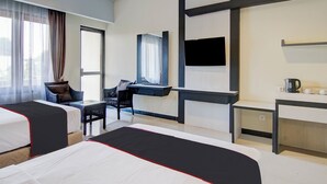 A modern hotel room with two beds, a desk, a chair, a TV, and a window with curtains. - Townhouse Oak Pekanbaru near Mall Pekanbaru formerly Hotel Grand Sahara (Pekanbaru)