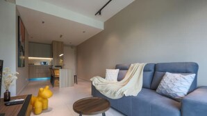 A modern living room with a blue sofa, a round wooden stool, and a yellow bear-shaped chair. - Residensi Majestic Maxim Condo (Kuala Lumpur)
